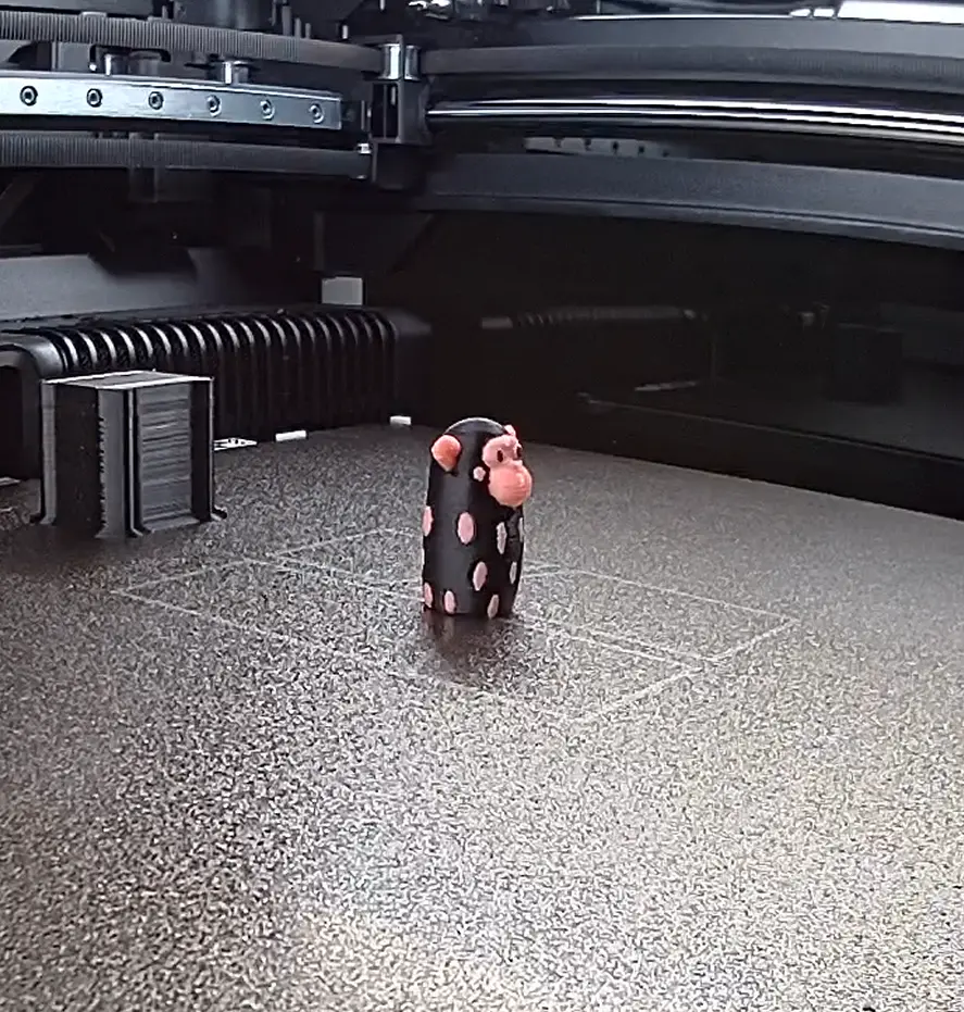Apró fekete-rózsaszín figura a 3D nyomtató tárgyasztalán